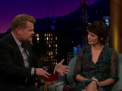 Lena Headey is sitting on the couch listening to James Corden.